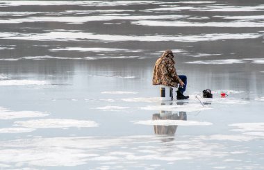 Cassopolis MI USA Mart 12020; Balıkçı eriyen bir gölde buzlu balık tutarken ters dönmüş bir kova üzerinde oturur