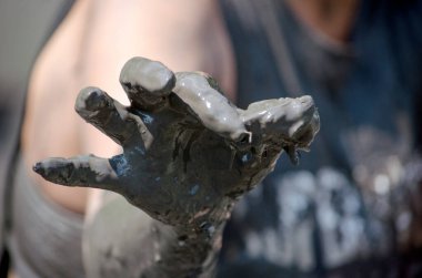 Çamurlu bir el, çamurla kaplı küçük bir kurbağa tutar.