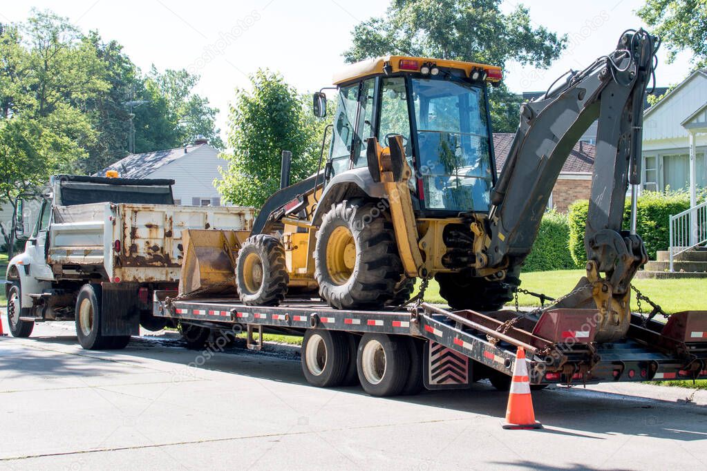 A dump truck delivers a front end loader back hoe on a trailer to a city street so that road work can begin