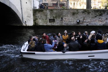 Belçika 'nın tarihi Bruges şehrinde 30 Kasım 2019' da kanaldaki bir teknede turistler.