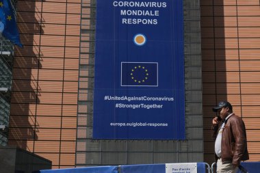 6 Mayıs 2020 'de Brüksel, Belçika' daki Avrupa Komisyonu genel merkezinin önünde koruyucu yüz maskesi takan bir yaya yürüyor.