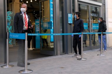 Bir güvenlik görevlisi 11 Mayıs 2020 'de Brüksel, Belçika' daki bir giyim mağazasına girmeden önce insanların kuyruğa girmesini kontrol ediyor..