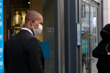 Bir güvenlik görevlisi 11 Mayıs 2020 'de Brüksel, Belçika' daki bir giyim mağazasına girmeden önce insanların kuyruğa girmesini kontrol ediyor..