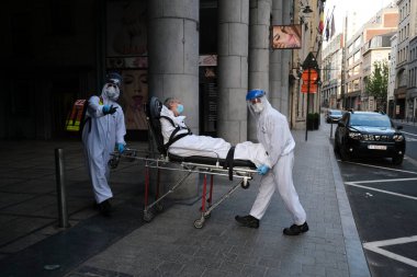 Kişisel koruma ekipmanı kullanan ilk yardım itfaiyecileri, Coronavirus hastalığı (COVID-19) şüphesiyle sedyeyle bir hastayı 16 Mayıs 2020 'de Brüksel, Belçika' da bir ambulansa ittiler.