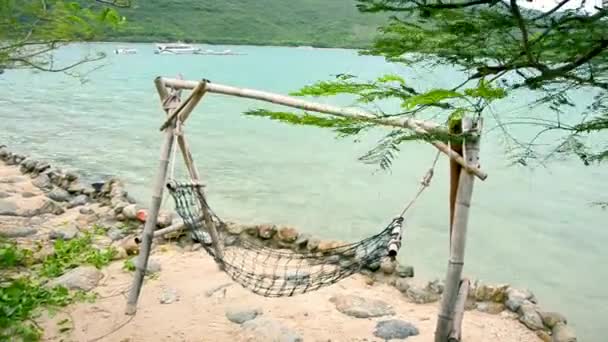 Di pantai laut, sebuah tempat tidur gantung pantai bergoyang dalam angin dan pada gelombang kecil. Di cakrawala pulau, kecepatan perahu, jet ski. Sebuah pulau yang menyenangkan untuk bersenang-senang dan bersantai . — Stok Video