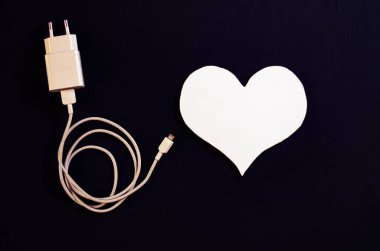 Üst manzara, siyah arka planda ahşap bir kalp dekoru ve şarj aleti. Sağlıklı bir kalbi koruma kavramı. Sevgililer Günü.