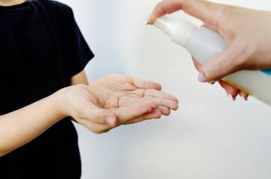 Ellerini dezenfektanla dezenfekte et ve ellerindeki virüsleri yok et. Elinde dezenfektan olan bir kadın eli ürünü küçük bir çocuğun ellerine püskürtüyor. Konsept:
