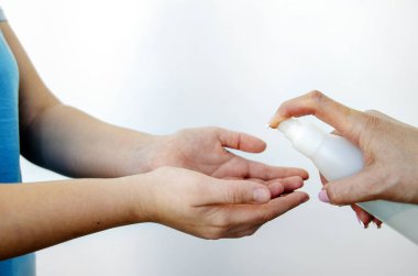 Ellerini dezenfektanla dezenfekte et ve ellerindeki virüsleri yok et. Elinde dezenfektanla sprey şişesi olan bir kadın eli ürünü bir çocuğun ellerine püskürtür. Konsept: