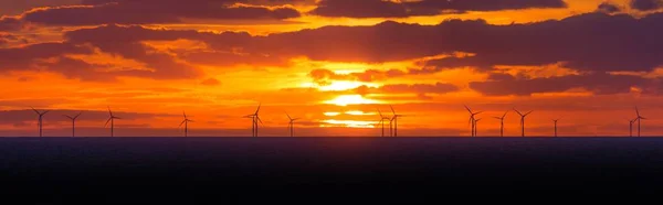 Panorama sunset sun at windmills offshore clean wind power farm