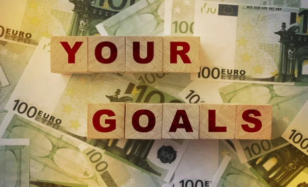 Your goals words letters on wooden cubes on 100 euro bills. Business and financial goal setting and achievements concept.