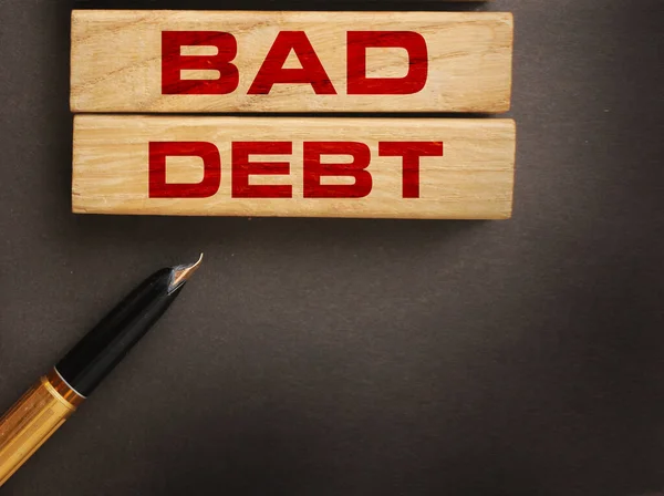 Bad debt on wooden blocks and luxury pen on dark grey background. Financial losses or business bankruptcy Concept .