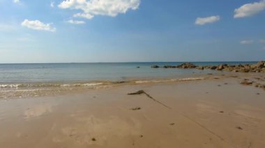 Tayland, Krabi 'deki Koh Lanta adasındaki Phra Ae plajındaki palmiye ağaçlarının altında tatil köyü yakınlarındaki denize doğru yürüyorum. Küçük dalgalar kayalık kıyılara sıçrayıp sıçrıyor. Güneşli bir gün. Tam HD.