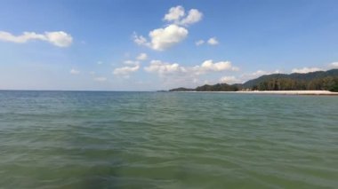 Tayland, Krabi 'deki Koh Lanta adasındaki Phra Ae plajındaki palmiye ağaçlarının altında deniz manzarası. Küçük dalgalar kayalık kıyılara sıçrayıp sıçrıyor. Güneşli bir gün. Tam HD.