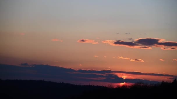 戏剧性的落日笼罩在小云和森林的树木之上 4K时差与红色紫色橙色粉红黄昏云天 戏剧化的天空和微小的云彩 明亮的橙色和红色的太阳下山了 — 图库视频影像