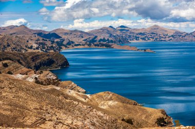 Isla del Sol, Titicaca Gölü, Comunidad Challa, Bolivya manzaralı. Peru ve Bolivya sınırındaki Titicaca Gölü manzarası. Büyük mavi göl, güneşli havada dramatik bulutlu gökyüzü.