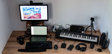 Ahşap masa üzerinde çalışma alanı, fotoğrafçı, film yapımcısı, yaratıcı tasarımcı. Boş bilgisayar ekranı, hoparlörleri, fotoğraf ekipmanları, kamera, lensler, lensler, akıllı telefon, piyano klavyesi olan yaratıcı tasarımcının yan görüntüsü. Evden, evden çalışmak.