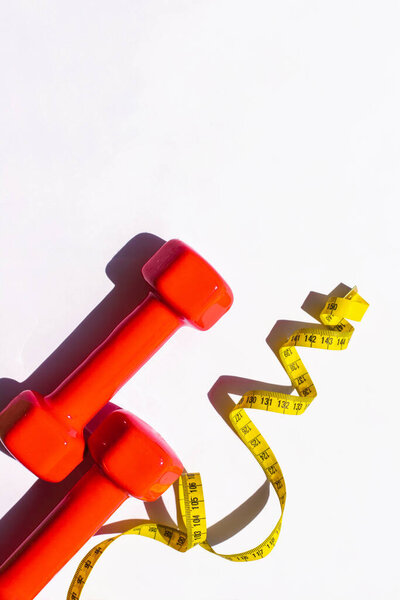 Red dumbbells and a centimeter-long yellow ribbon on a white background. Athletic activity.Fitness at home.Diet.