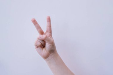 Bir çocuğun eli, beyaz arka planda bir zafer jesti gösterir. İki parmak yukarı..