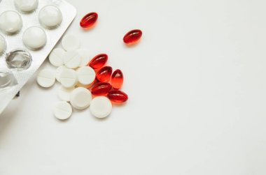 Beyaz tabletler ve kırmızı kapsüller beyaz arka plana saçılmıştır. Farklı dozaj formları. Tıbbi ürünlerden ambalaj.