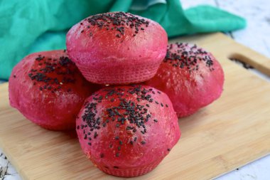 Homemade beetroot bread buns with black sesame seeds on wooden board 