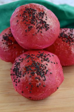 Homemade beetroot bread buns with black sesame seeds on wooden board 