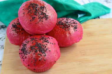 Homemade beetroot bread buns with black sesame seeds on wooden board