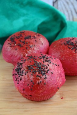 Homemade beetroot bread buns with black sesame seeds on wooden board 