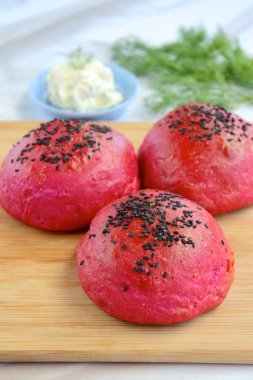 Homemade beetroot bread buns with black sesame seeds on wooden board 