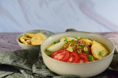 Soto Ayam, yellow turmeric chicken soup with vermicelli noodles, shredded chicken, boiled egg, fried potato, sprouts, tomato, parsley and fried shallots, served with Emping. Popular Indonesian food