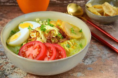 Soto Ayam, yellow turmeric chicken soup with vermicelli noodles, shredded chicken, boiled egg, fried potato, sprouts, tomato, parsley and fried shallots, served with Emping. Popular Indonesian food
