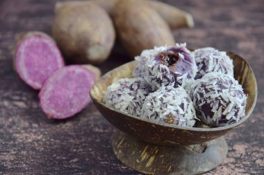 Klepon Ubi Ungu, kurutulmuş hindistan ceviziyle kaplı palmiye şekeriyle doldurulmuş mor patates glüten pirinç topları. Ahşap arkaplan