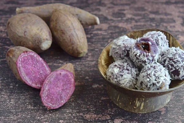 Klepon Ubi Ungu, kurutulmuş hindistan ceviziyle kaplı palmiye şekeriyle doldurulmuş mor patates glüten pirinç topları. Ahşap arkaplan