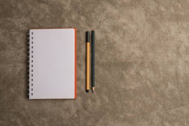 Kahverengi arka planda defter, kalem ve kalem. Üst görünüm ve boşluk kopyala. Metni ortaya koymak için boş defter sayfası