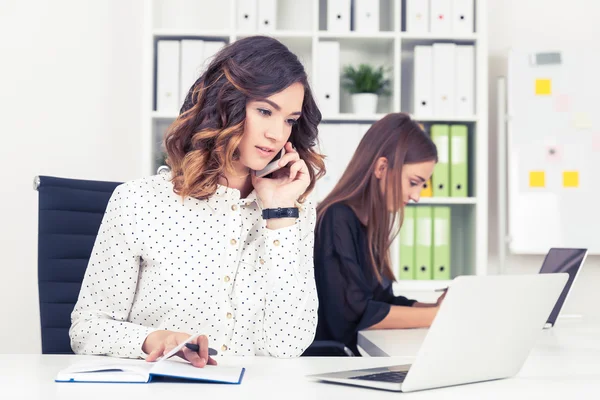 Una joven seria con camisa de polka está hablando con el cliente. Su colega está leyendo en segundo plano. Concepto de vida de oficina — Foto de Stock