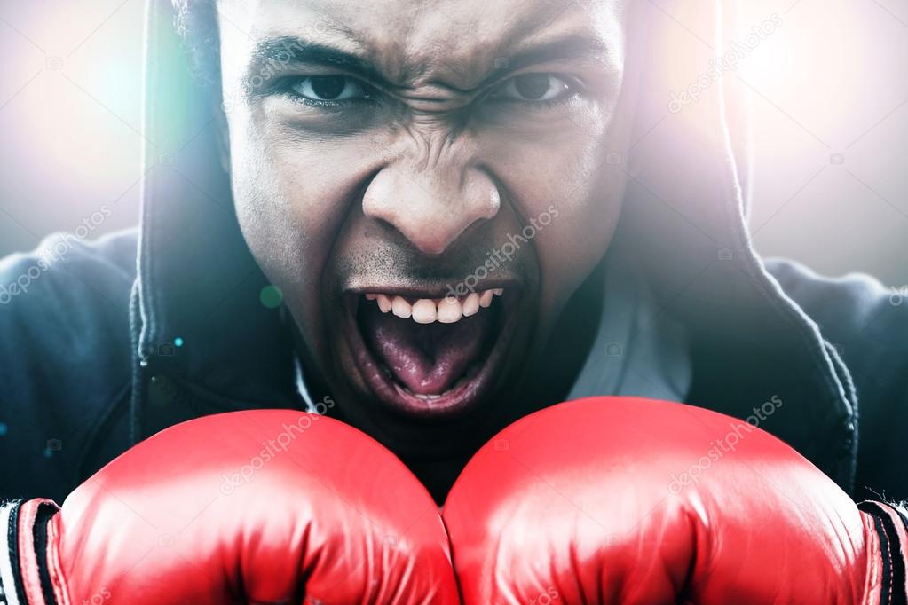 Close up of enraged African American man in boxing gloves. Concept of championship 