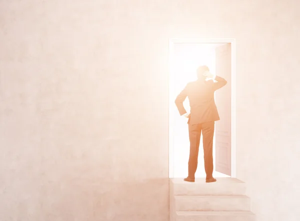 Empresário perto da porta aberta na parede iluminada pelo sol com escadas — Fotografia de Stock