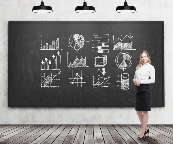 Smiling blond businesswoman with graphs on blackboard — Stock Photo, Image