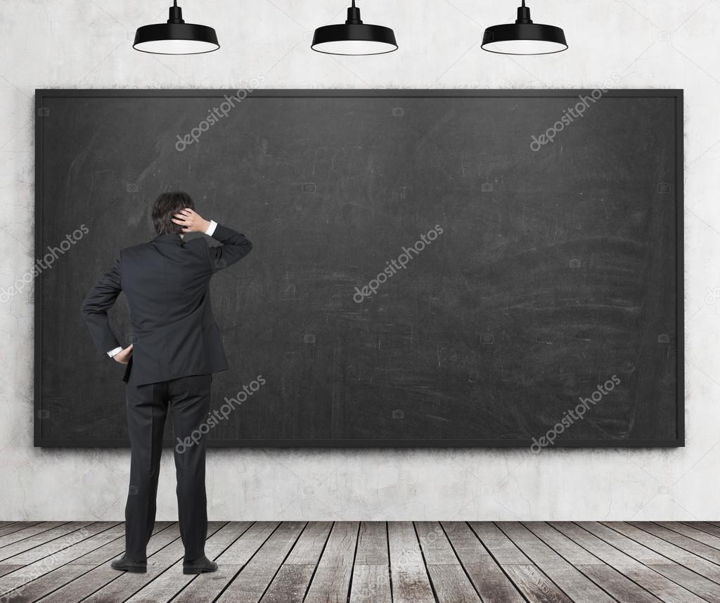 Man in suit looking at empty blackboard