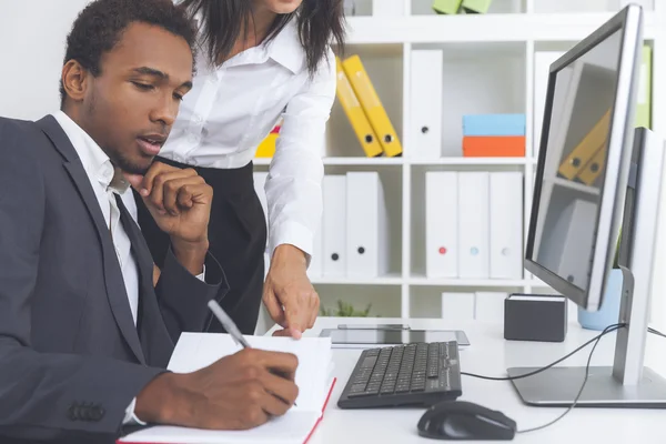 El jefe está escribiendo en cuaderno naranja. Su asistente está de pie junto a él y señalando una línea. Concepto de colaboración —  Fotos de Stock