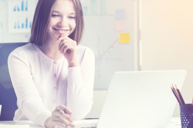 Ofiste dizüstü bilgisayar kullanan gülümseyen kadın.