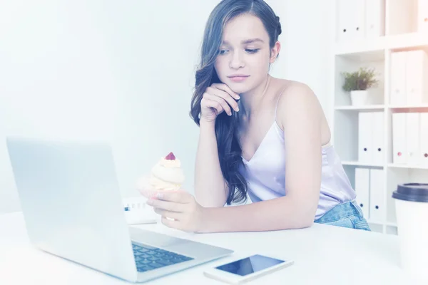 Girl in doubt with cupcake in office