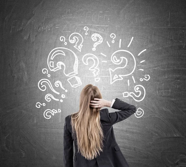 Woman scratching head and question marks on blackboard — Stock Photo, Image