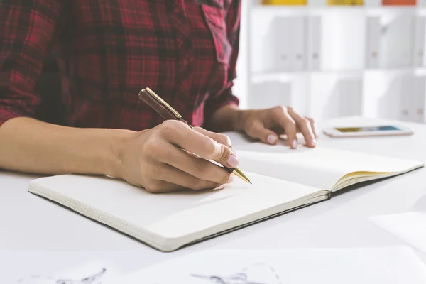 Primo piano delle mani delle donne che scrivono in un grande quaderno disteso sulla talle in un ufficio bianco. Concetto di morire arte della scrittura a mano — Foto Stock