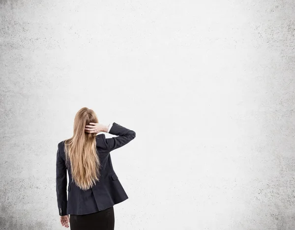 Woman scratching head looking at concrete wall — Stok fotoğraf
