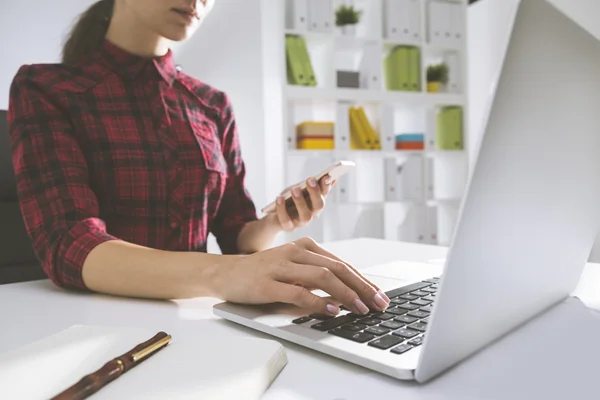 Woman in red checkered shirt is working at her laptop and holdin — Stockfoto