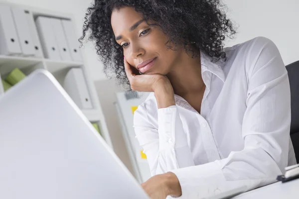 Dreamy young woman in empty office looking at her laptop screen — Stock Photo, Image