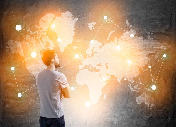 Man in T-shirt standing near blackboard with world map — Stock Photo, Image