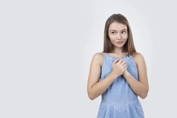 Застенчивая девушка в синем платье стоит на сером фоне — стоковое фото