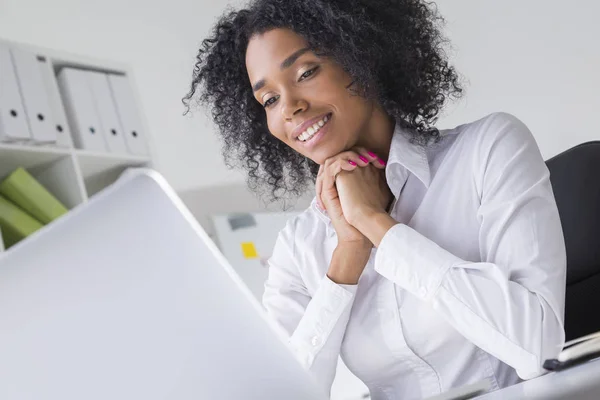Veselá žena z Afriky se dívá na obrazovku přenosného počítače v kanceláři — Stock fotografie