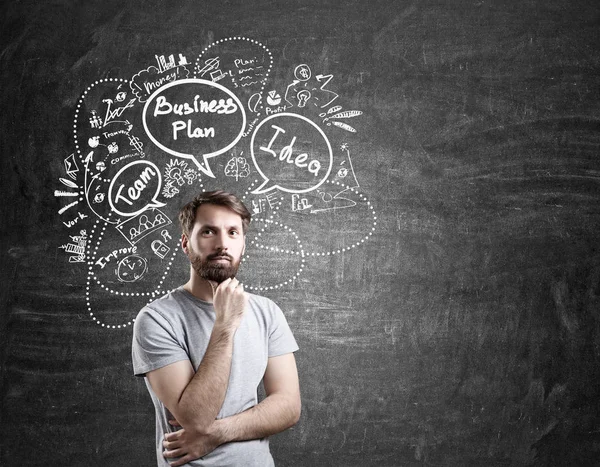 Man in T-shirt and business plan sketches on blackboard — Stock Photo, Image